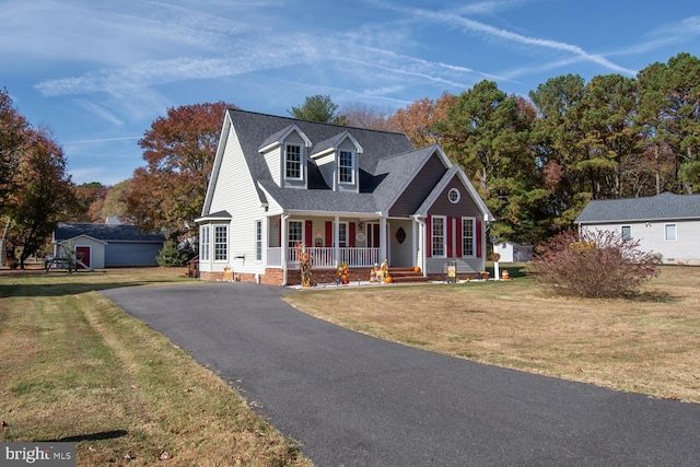 new england style home with covered porch, a front yard, and an outdoor structure