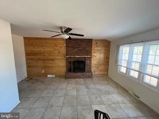 unfurnished living room featuring wood walls, ceiling fan, and a brick fireplace