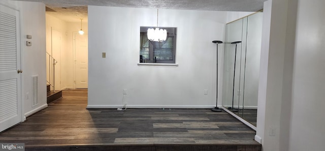 corridor with a textured ceiling, an inviting chandelier, and dark wood-type flooring