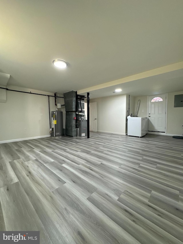 basement featuring water heater, heating unit, washer and clothes dryer, and light hardwood / wood-style flooring