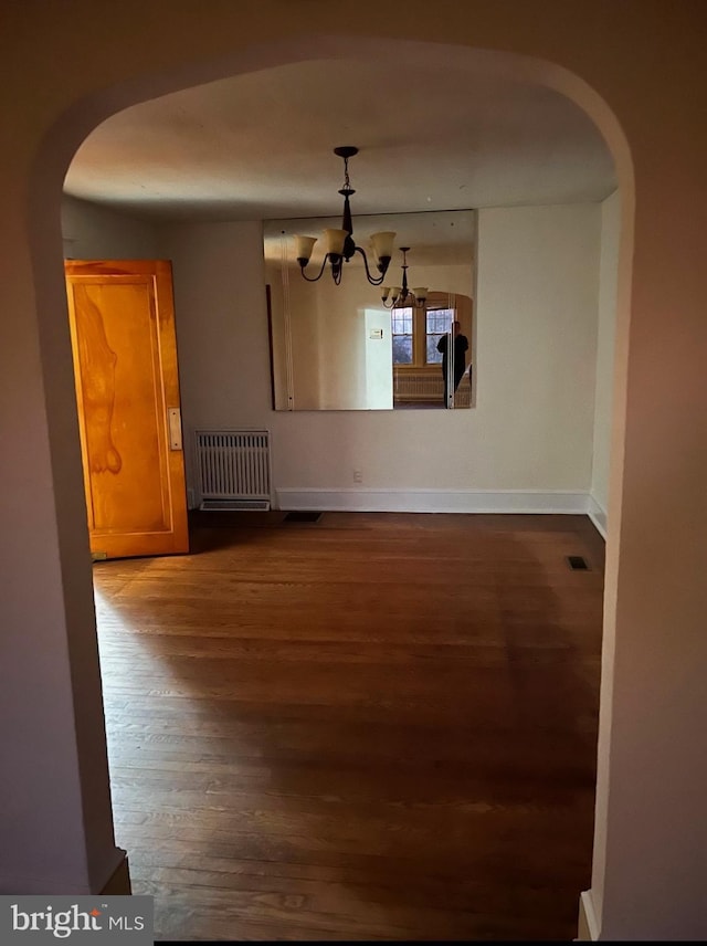 unfurnished dining area with radiator, dark wood-style floors, a chandelier, arched walkways, and baseboards
