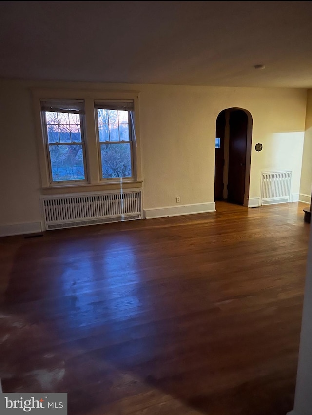 empty room with radiator, arched walkways, and dark wood-style flooring