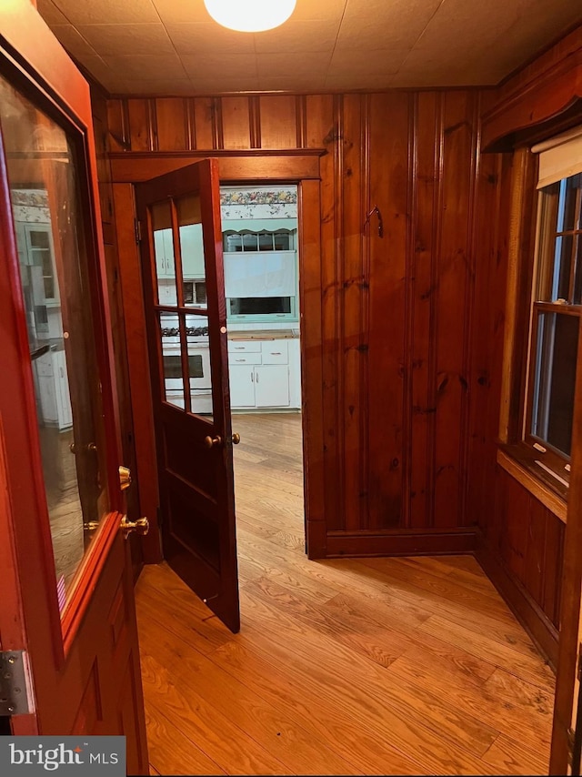 corridor with light wood-type flooring and wooden walls