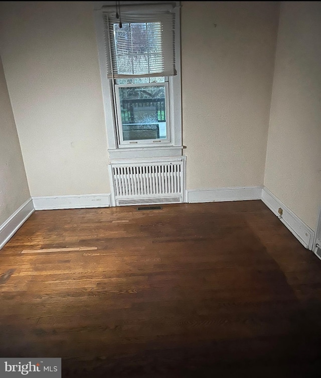 empty room featuring baseboards, wood finished floors, and radiator heating unit