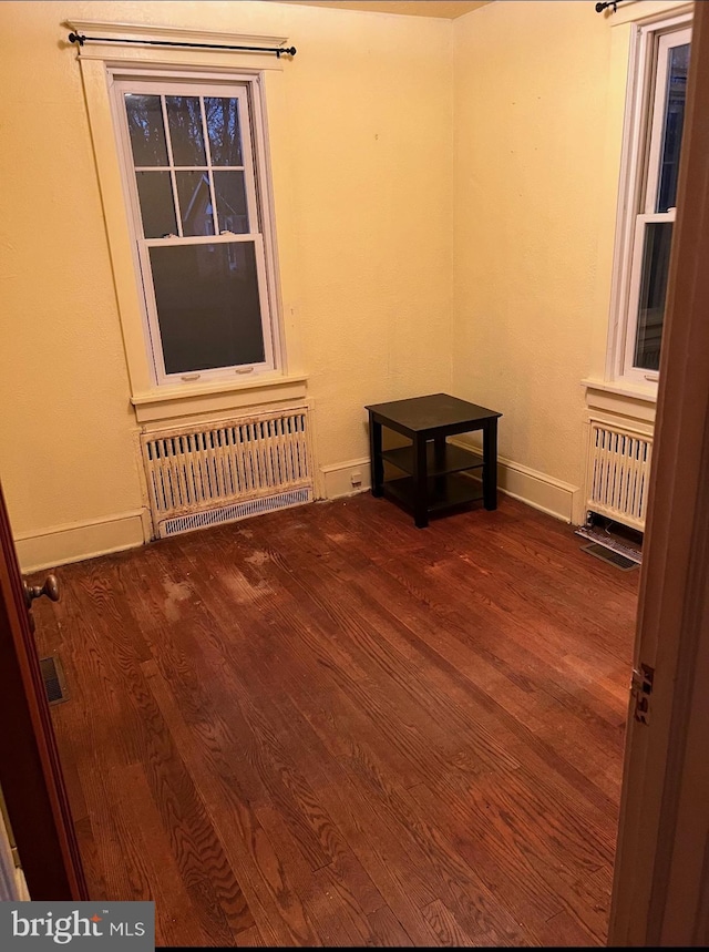 empty room featuring radiator, dark wood finished floors, and baseboards