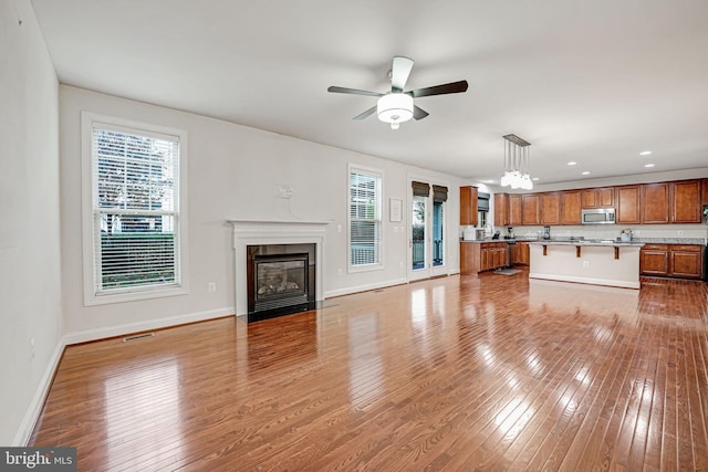 unfurnished living room featuring ceiling fan with notable chandelier and light hardwood / wood-style floors