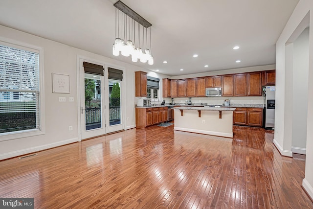 kitchen with a center island, hanging light fixtures, stainless steel appliances, hardwood / wood-style floors, and a breakfast bar area