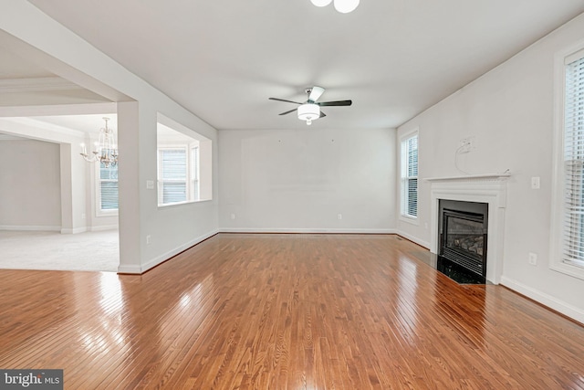 unfurnished living room featuring ceiling fan with notable chandelier, hardwood / wood-style flooring, and a healthy amount of sunlight