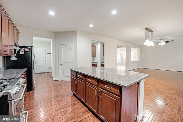 kitchen featuring hanging light fixtures, high end stainless steel range oven, light stone counters, light hardwood / wood-style floors, and a kitchen island