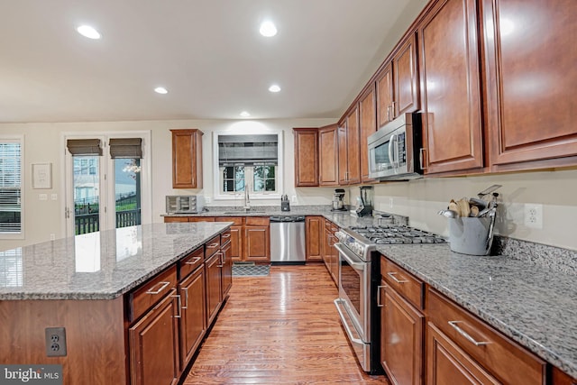 kitchen featuring sink, light wood-type flooring, a kitchen island, light stone counters, and stainless steel appliances