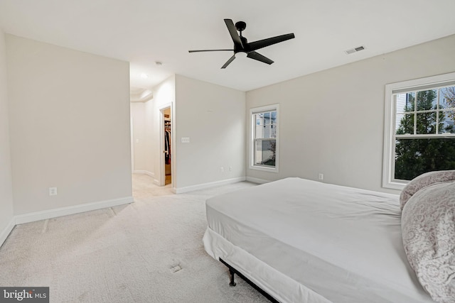 bedroom with a walk in closet, ceiling fan, a closet, and light colored carpet