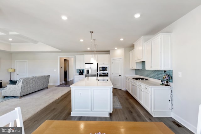 kitchen featuring sink, appliances with stainless steel finishes, dark hardwood / wood-style floors, hanging light fixtures, and a kitchen island with sink