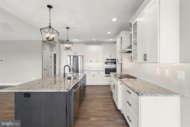 kitchen featuring appliances with stainless steel finishes, sink, a large island with sink, white cabinetry, and hanging light fixtures