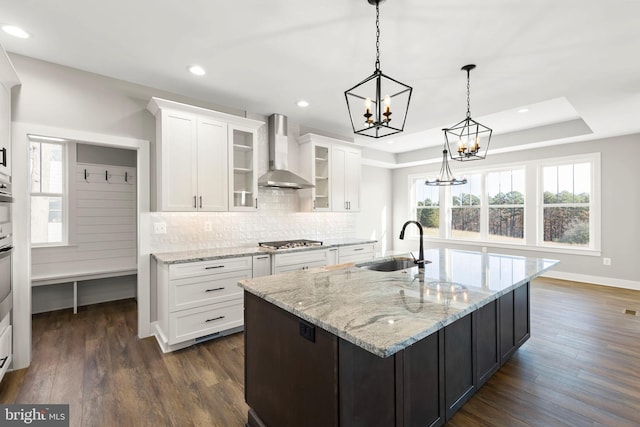 kitchen featuring pendant lighting, a raised ceiling, sink, wall chimney exhaust hood, and white cabinetry