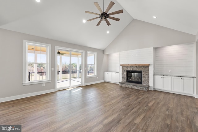 unfurnished living room featuring wood-type flooring, high vaulted ceiling, a stone fireplace, and ceiling fan