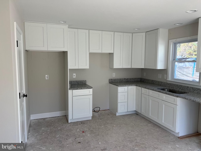 kitchen with dark stone countertops, white cabinetry, and sink