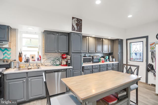 kitchen with stainless steel appliances, backsplash, light wood-type flooring, gray cabinets, and sink