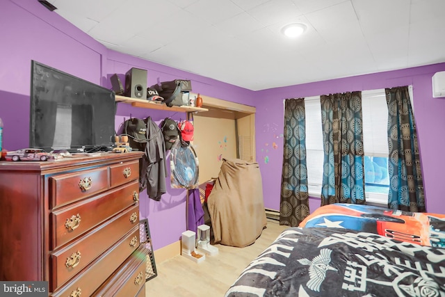 bedroom with a wall mounted AC and light hardwood / wood-style floors