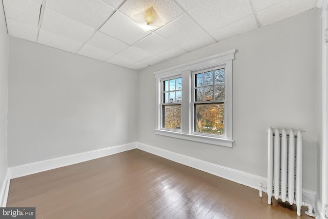 empty room featuring a drop ceiling, dark wood-type flooring, and radiator