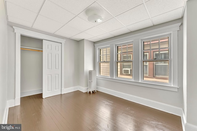 unfurnished bedroom with radiator heating unit, a paneled ceiling, hardwood / wood-style flooring, and a closet