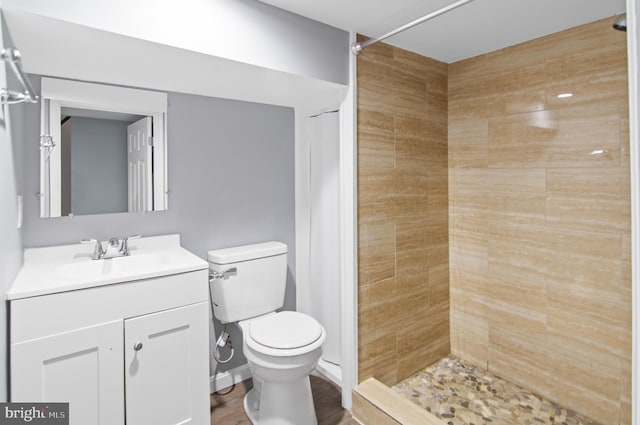 bathroom with hardwood / wood-style flooring, vanity, toilet, and tiled shower