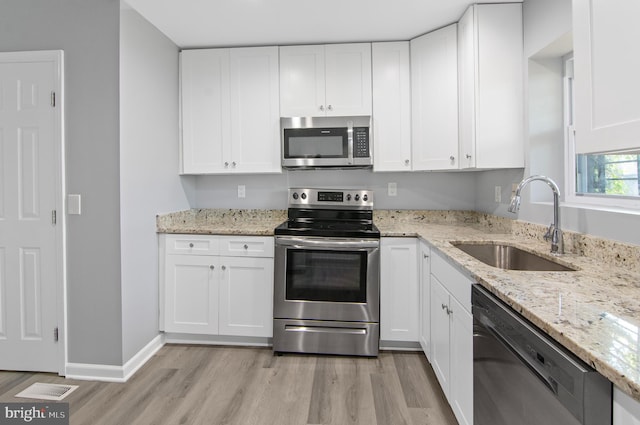 kitchen with white cabinets, stainless steel appliances, sink, and light hardwood / wood-style flooring