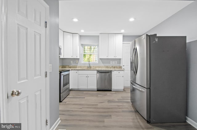 kitchen with stainless steel appliances, sink, light stone countertops, white cabinetry, and light hardwood / wood-style flooring