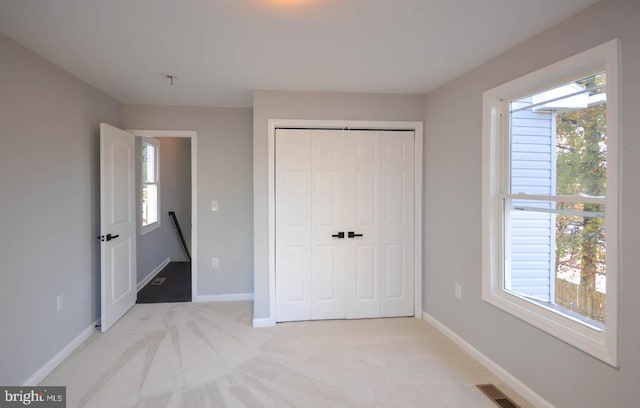 unfurnished bedroom with light colored carpet, multiple windows, and a closet