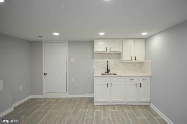 kitchen with white cabinets, light wood-type flooring, decorative backsplash, and sink