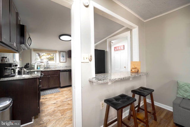 kitchen featuring stainless steel appliances, dark brown cabinets, light stone countertops, sink, and a breakfast bar area