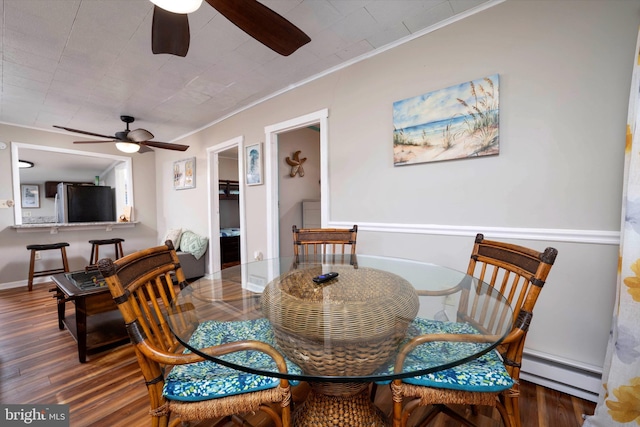 dining room featuring dark wood-type flooring, baseboard heating, ceiling fan, and ornamental molding