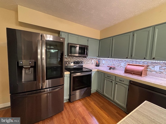 kitchen featuring green cabinetry, light hardwood / wood-style flooring, a textured ceiling, appliances with stainless steel finishes, and tasteful backsplash