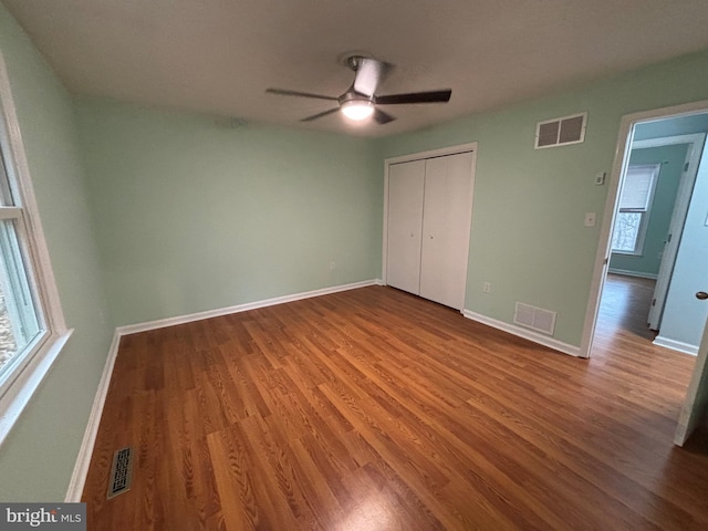 unfurnished bedroom featuring multiple windows, hardwood / wood-style floors, a closet, and ceiling fan