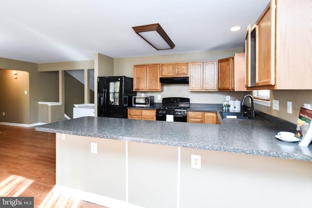 kitchen featuring black appliances, light wood-type flooring, kitchen peninsula, and sink