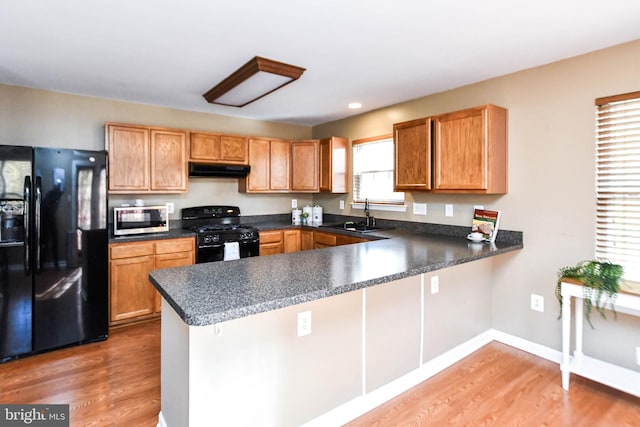 kitchen with black appliances, sink, kitchen peninsula, and wood-type flooring