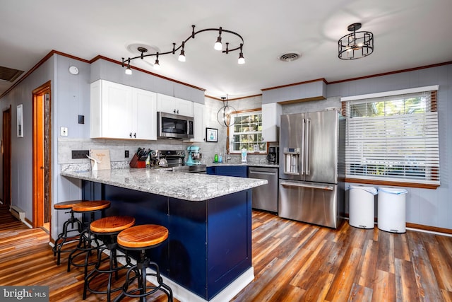 kitchen featuring white cabinets, ornamental molding, appliances with stainless steel finishes, dark hardwood / wood-style flooring, and kitchen peninsula