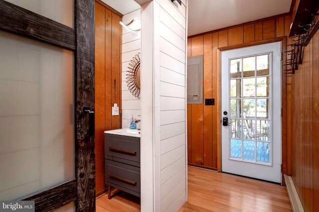 doorway to outside with electric panel, light hardwood / wood-style floors, and wooden walls