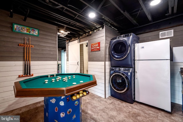 recreation room featuring concrete flooring, wooden walls, and stacked washer / drying machine