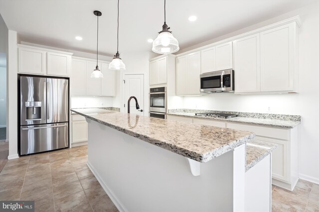 kitchen featuring hanging light fixtures, a kitchen island with sink, light stone countertops, white cabinetry, and appliances with stainless steel finishes