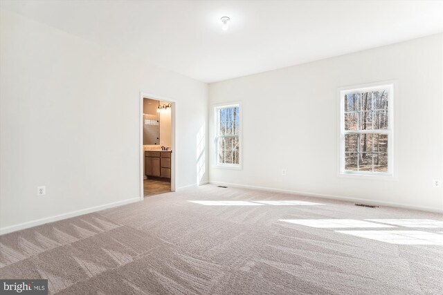 unfurnished bedroom with ensuite bath and light colored carpet