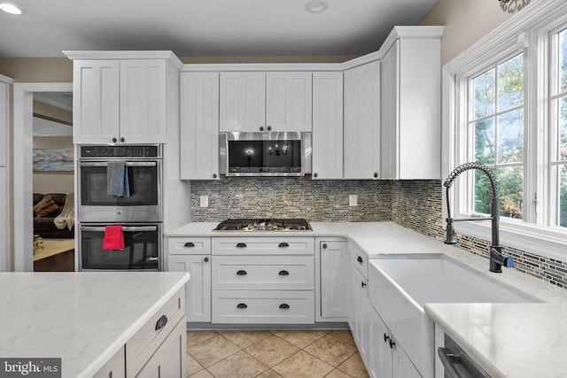 kitchen with tasteful backsplash, stainless steel appliances, white cabinetry, light tile patterned floors, and sink