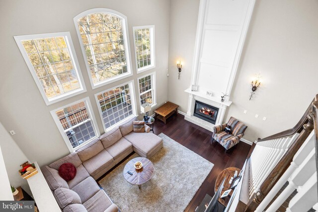 living room with dark wood-type flooring, a towering ceiling, and a large fireplace