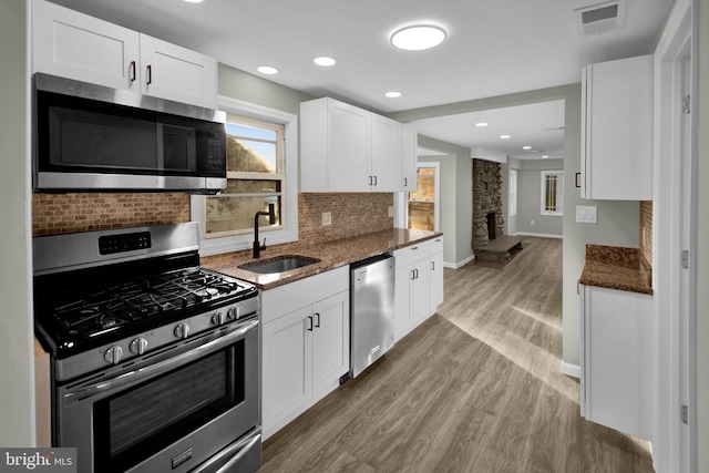 kitchen featuring light hardwood / wood-style floors, appliances with stainless steel finishes, sink, white cabinets, and dark stone counters