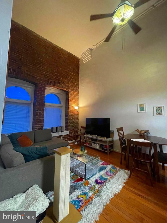 living room featuring wood-type flooring, ceiling fan, and brick wall