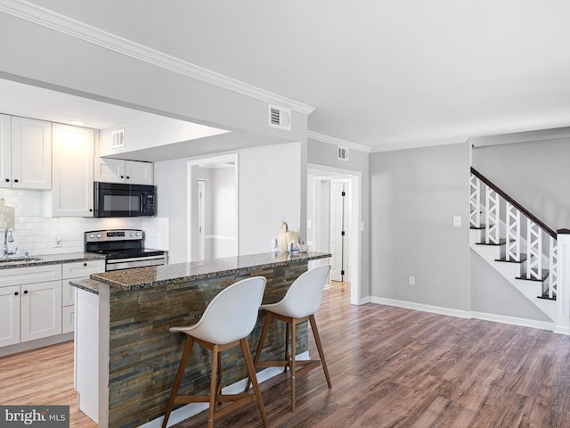 kitchen with stainless steel electric range, dark stone counters, white cabinets, a breakfast bar area, and light wood-type flooring