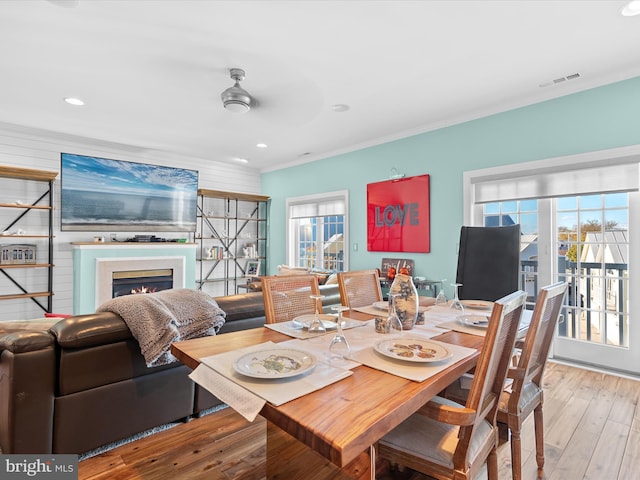 dining area with ceiling fan, wood walls, wood-type flooring, and crown molding