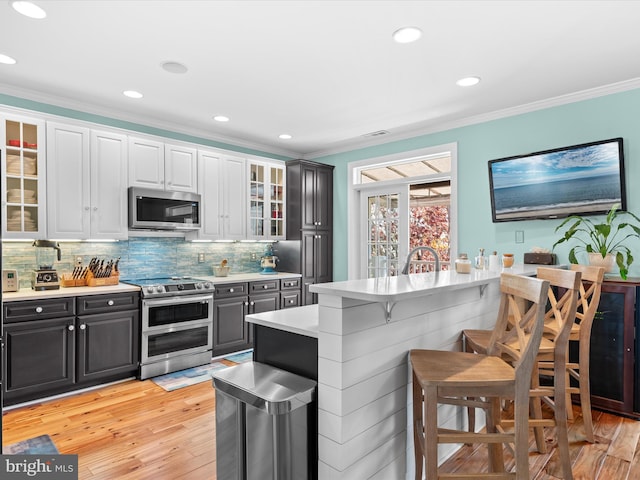 kitchen featuring white cabinets, stainless steel appliances, light hardwood / wood-style flooring, and crown molding