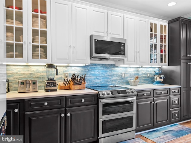 kitchen with white cabinets, light wood-type flooring, stainless steel appliances, and backsplash