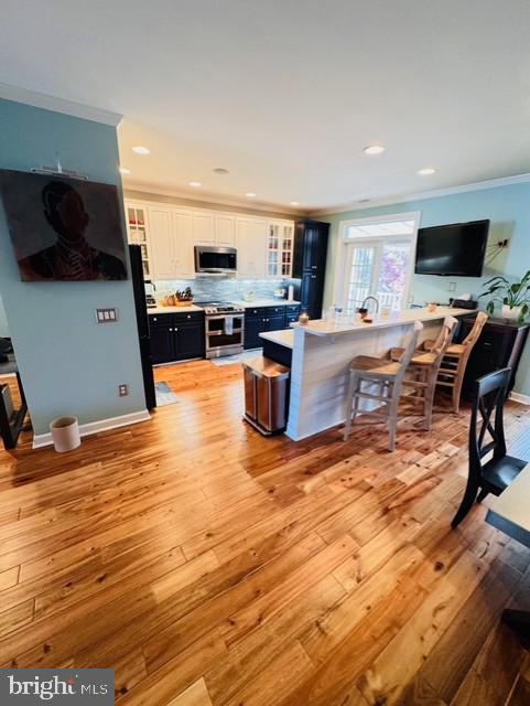 kitchen featuring white cabinetry, stainless steel appliances, light hardwood / wood-style flooring, a breakfast bar, and ornamental molding