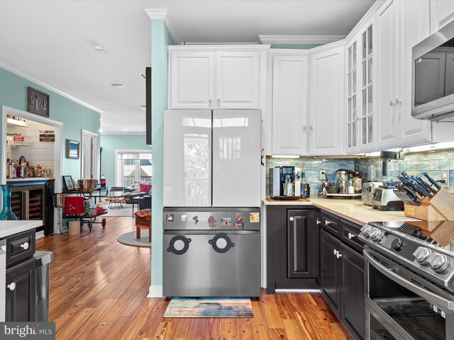 kitchen with white cabinets, backsplash, appliances with stainless steel finishes, and light hardwood / wood-style flooring